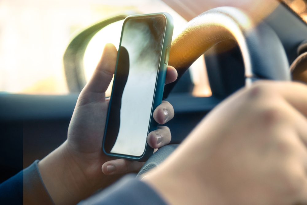 Close-up of driver's hands using a cell phone while operating a vehicle