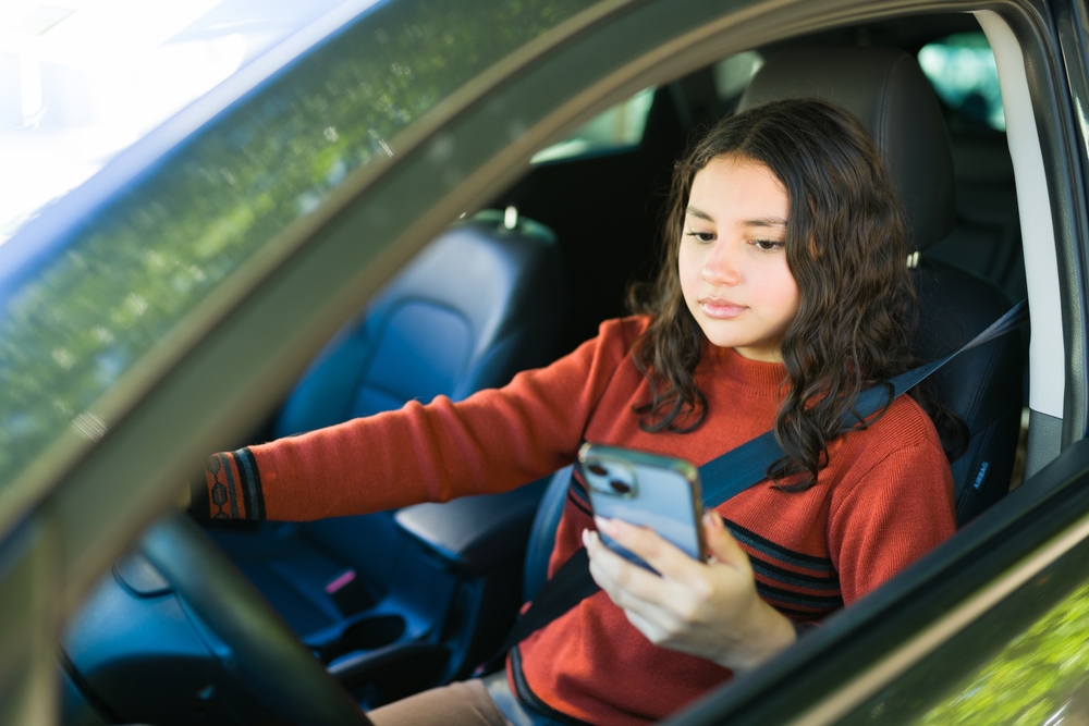 View through driver's window of young woman using cell phone