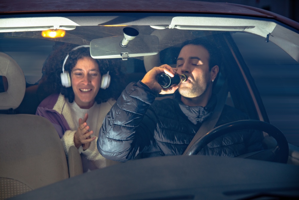 Driver consuming a beer while operating a vehicle with passenger in back